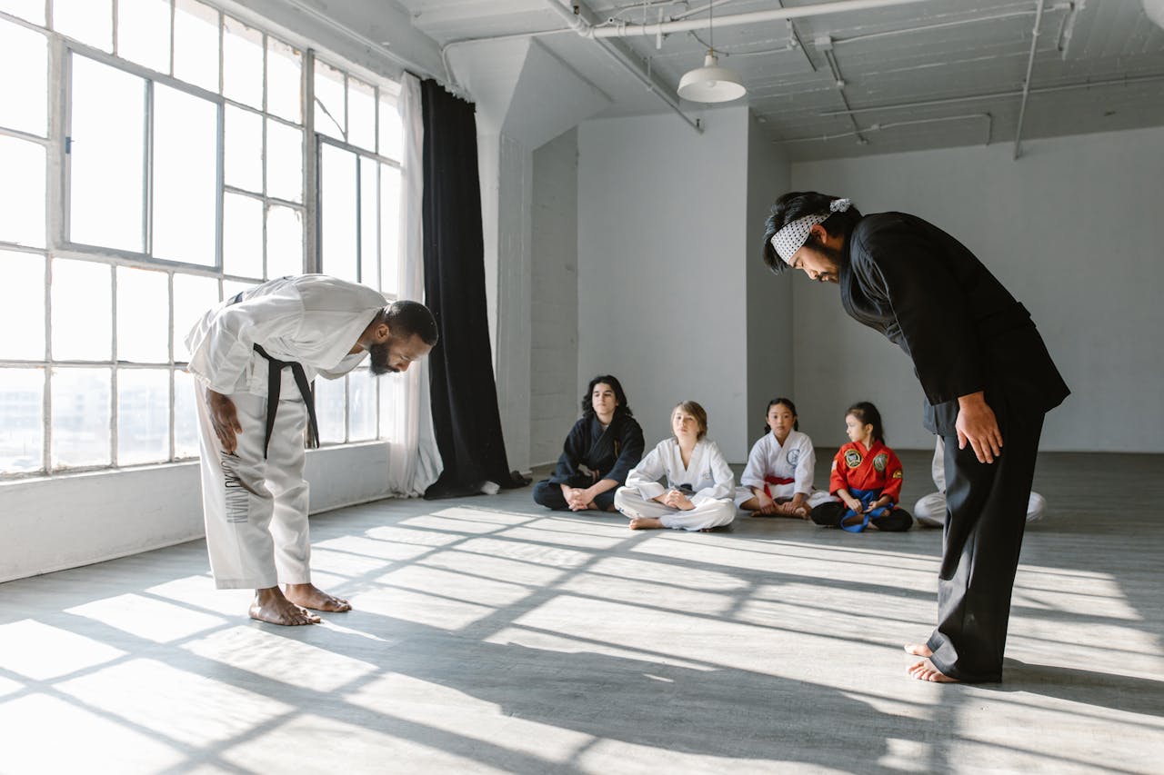 Martial arts practitioners in a dojo bowing as students watch, emphasizing discipline.